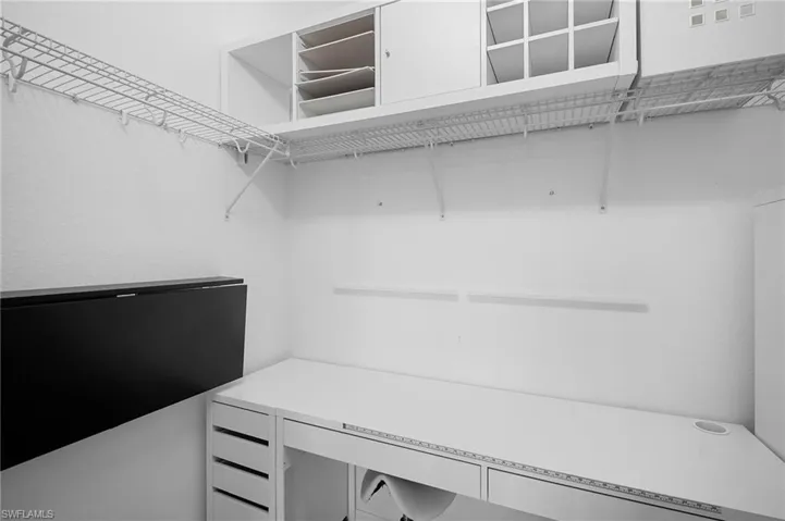Dedicated workspace featuring a built-in desk with drawers, white wall shelving, wire shelving, and an integrated wall-mounted folding surface