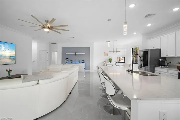 Open-concept living area featuring large format tile flooring, a spacious kitchen island with seating, a stainless steel French door refrigerator, white shaker cabinetry, and recessed lighting throughout