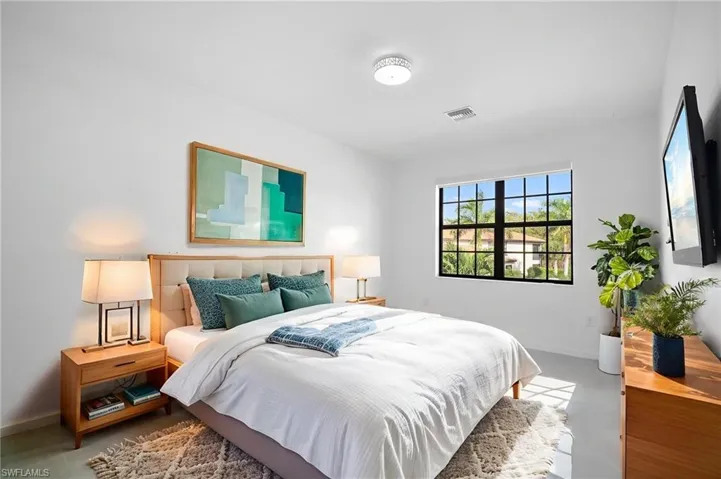 Spacious bedroom featuring light-toned flooring, a large window with black grilles, and a ceiling-mounted light fixture