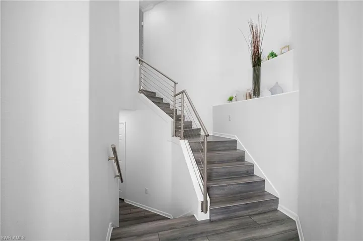 Staircase featuring wood-finish treads, stainless steel cable railing, and a built-in wall niche with shelving