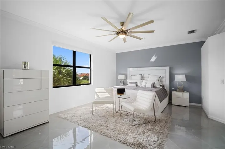 Spacious room featuring large format tile flooring, crown molding, a window with exterior foliage, and a contemporary ceiling fan with integrated lighting
