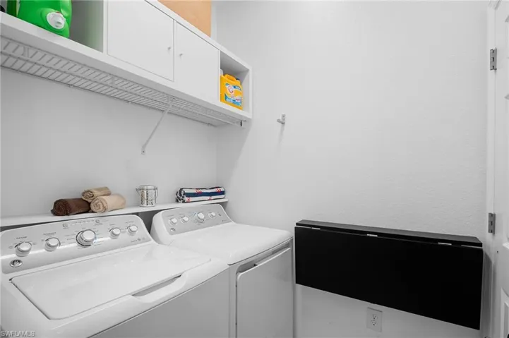 Dedicated laundry area featuring a wall-mounted drying rack, white cabinetry, open shelving, and a folding table