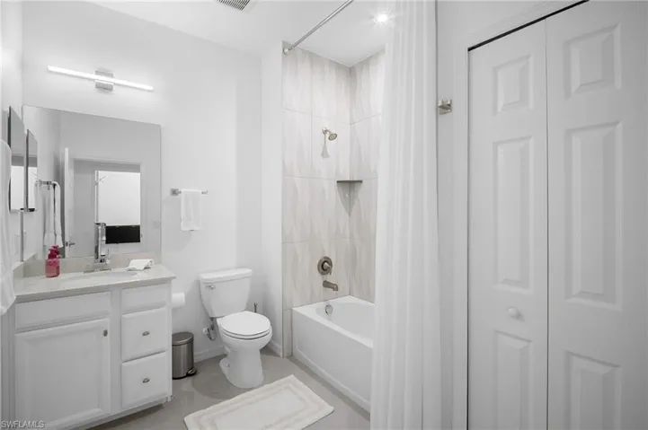 Full bathroom featuring a single vanity with stone-finish countertop, white cabinetry, a bathtub with shower, patterned wall tile, and bifold closet doors