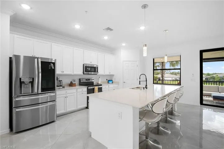 Contemporary kitchen featuring white cabinetry, stainless steel appliances, a large island with seating, pendant lighting, and tile flooring