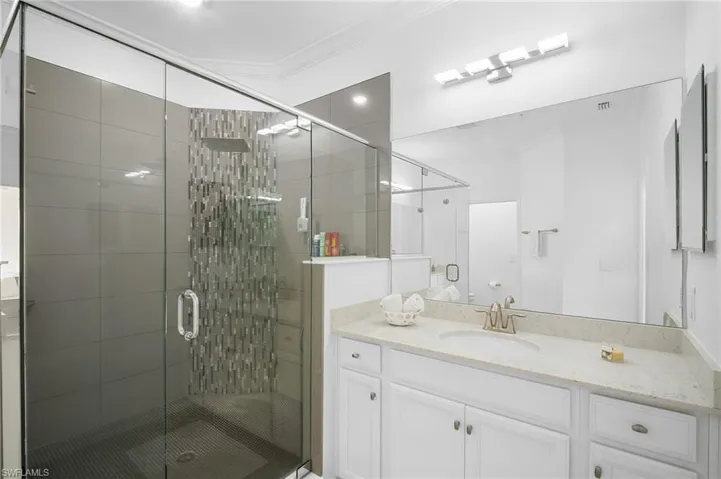 Glass-enclosed shower with a rainfall showerhead, neutral-toned wall tiles, and an accent mosaic tile strip