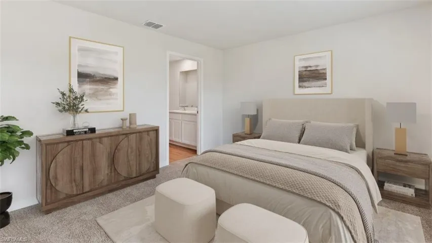 Carpeted bedroom featuring neutral wall tones, a built-in air vent, and a doorway opening to a bathroom with a dual vanity