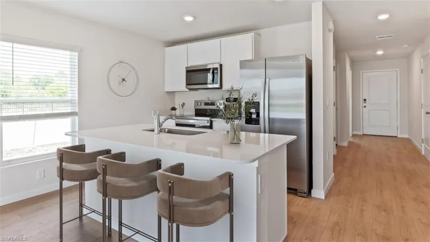 Open-concept kitchen featuring a large island with seating, stainless steel appliances, white cabinetry, wood-finish flooring, and recessed lighting