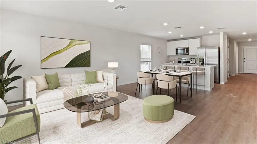 Open-concept living space featuring wood-finish flooring, recessed lighting, and a kitchen with stainless steel appliances, white cabinetry, and an eat-at island