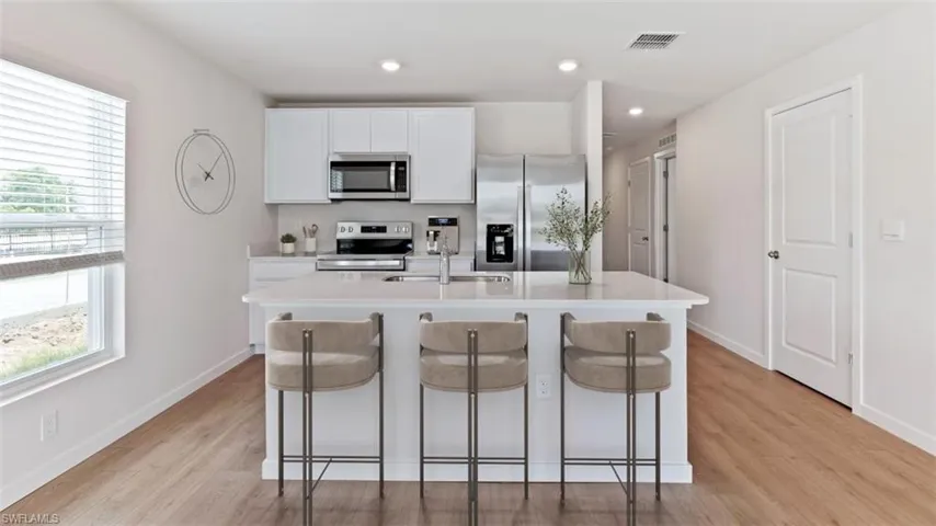 Modern kitchen featuring a large island with seating, stainless steel appliances, white cabinetry, wood-finish flooring, and recessed lighting