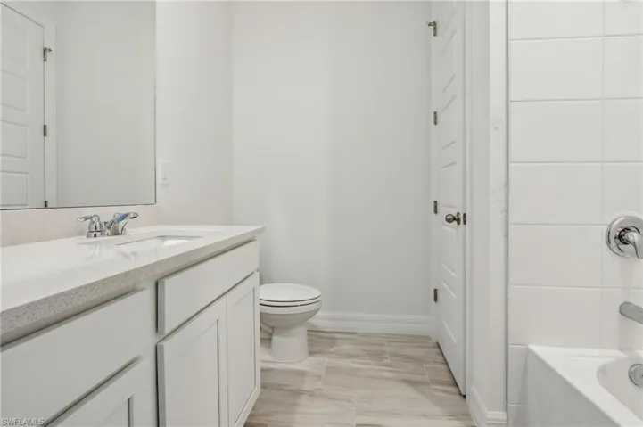 Bathroom with toilet, shower / tub combination, vanity, and baseboards