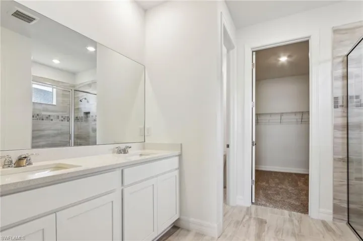 Full bathroom featuring double vanity, a stall shower, a spacious closet, visible vents, and a sink