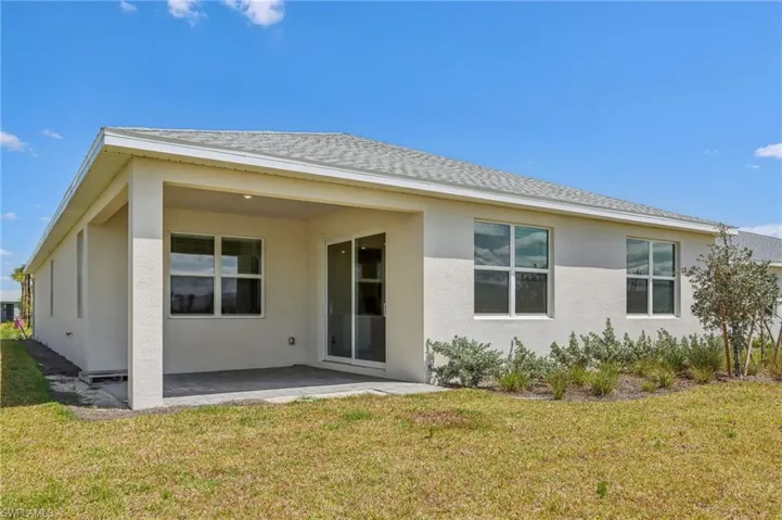 Back of house featuring a yard, stucco siding, a patio area, and roof with shingles
