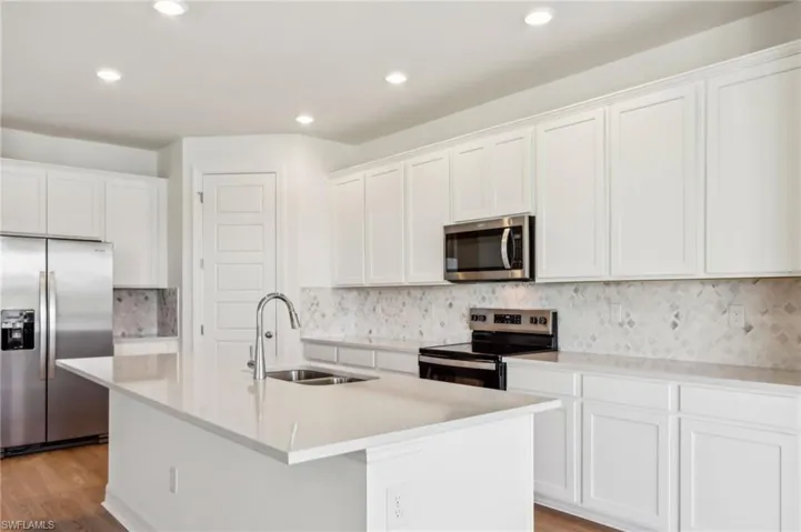 Kitchen with white cabinetry, recessed lighting, a sink, stainless steel appliances, and a center island with sink