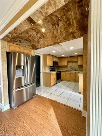 Kitchen featuring wood-finish cabinetry, stainless steel refrigerator, black range, built-in microwave, and tile flooring
