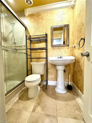 Bathroom featuring a glass-enclosed shower, pedestal sink, and patterned wall covering