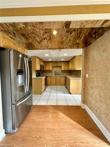 Kitchen featuring wood-finish flooring, a stainless steel refrigerator, light wood cabinetry, and a tiled kitchen floor
