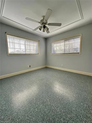 Room featuring a ceiling fan with integrated lighting, recessed ceiling detail, light-toned walls, and speckled flooring