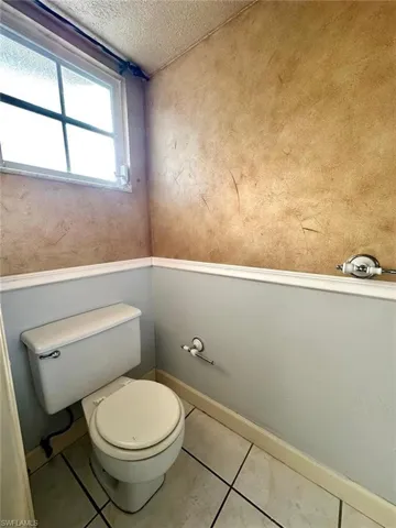 Compact bathroom featuring a white toilet, tile flooring, and a textured wall finish
