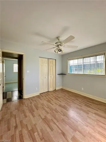 Spacious room featuring wood-finish flooring, light blue walls, and a ceiling fan with integrated lighting