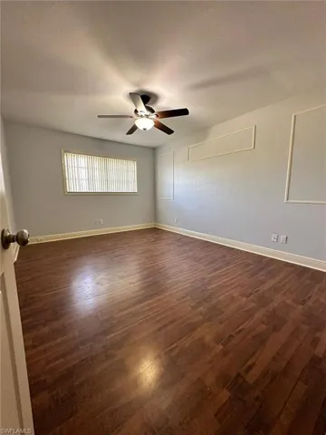 Spacious room featuring wood-finish flooring, a ceiling fan with integrated lighting, a window with horizontal blinds, and decorative wall molding