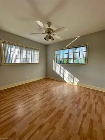 Spacious interior featuring wood-finish flooring, two windows with horizontal blinds, a white ceiling fan with integrated lighting, and a light-toned wall color