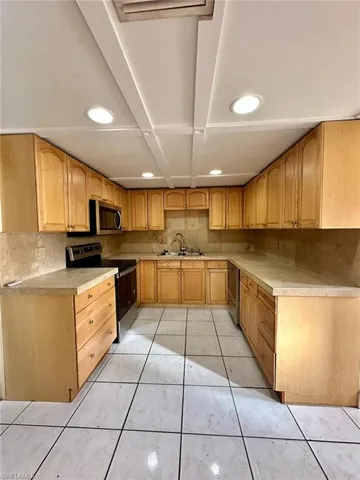 Kitchen featuring U-shaped cabinetry with light wood-finish doors, light-toned countertops, and a tiled backsplash