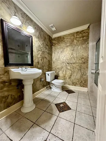 Pedestal sink with fluted base, framed mirror with integrated lighting fixture, and tile flooring featuring mosaic accents
