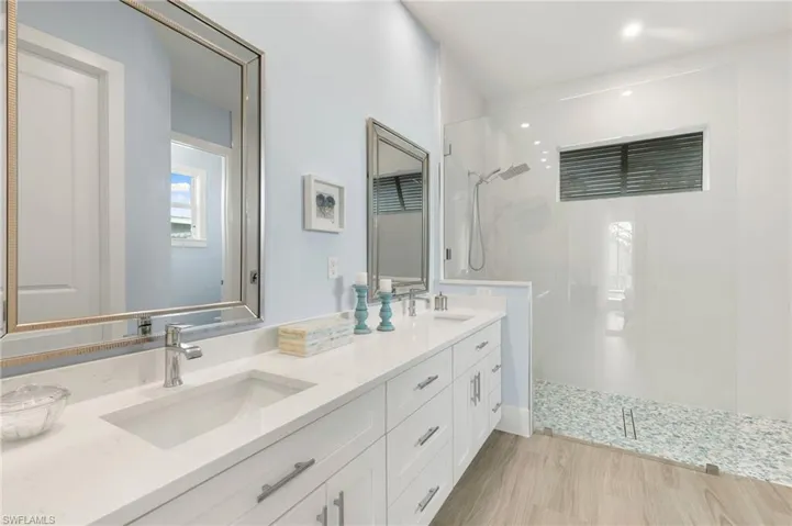 Primary bath with dual sinks, tile flooring, doorless glass walled walk-in shower