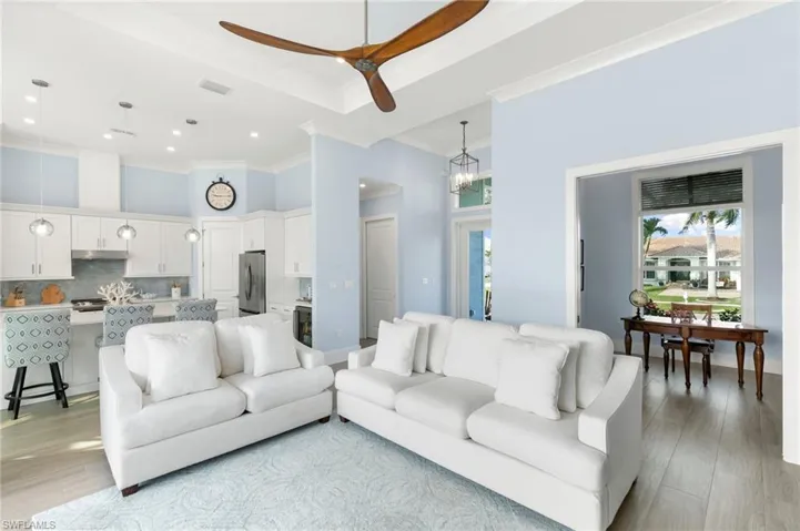 Living room with light wood style porcelain tile flooring, a high ceiling, kitchen in background and den on right in background