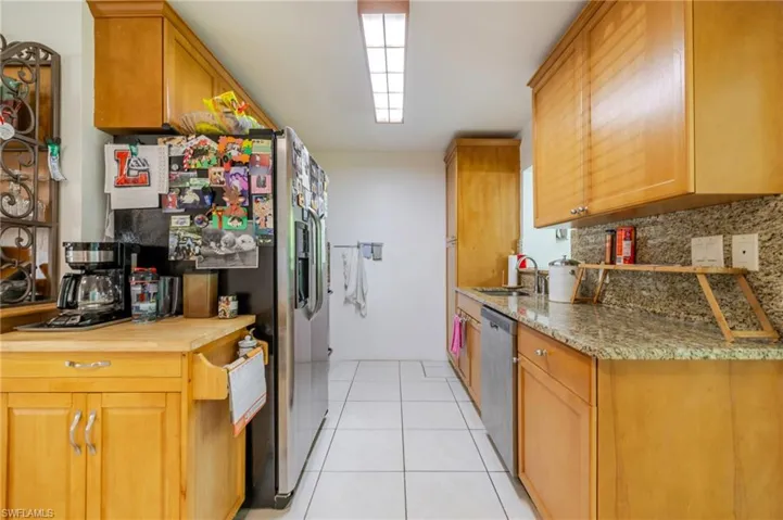Kitchen featuring backsplash, light tile patterned floors, stainless steel appliances, brown cabinets, and butcher block countertops