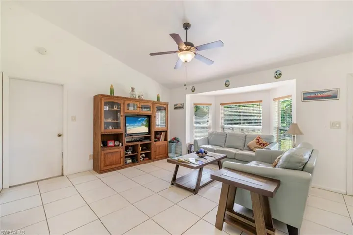 Living room featuring light tile patterned floors, ceiling fan, and vaulted ceiling
