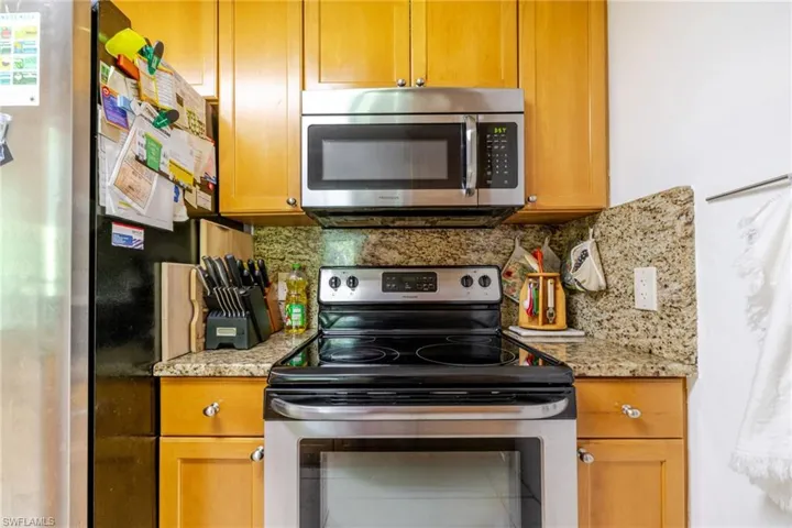 Kitchen featuring appliances with stainless steel finishes, backsplash, brown cabinetry, and light stone counters