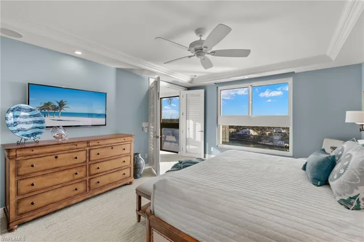 Bedroom with crown molding, light colored carpet, access to exterior, a ceiling fan, and a raised ceiling