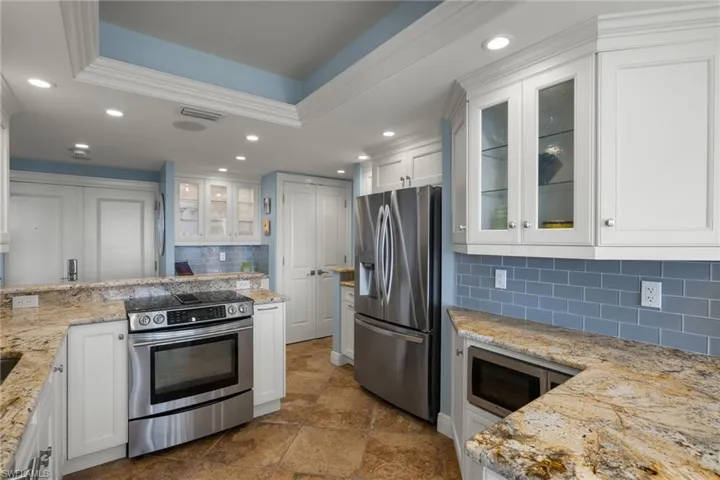 Kitchen with glass insert cabinets, white cabinetry, appliances with stainless steel finishes, light stone countertops, and recessed lighting