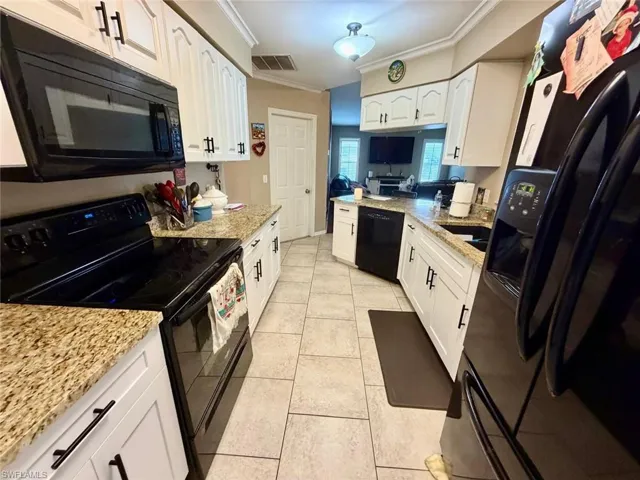 Kitchen with black appliances, white cabinets, light stone countertops, ornamental molding, and light tile patterned floors