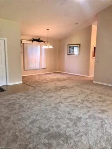 Carpeted empty room featuring vaulted ceiling and a chandelier