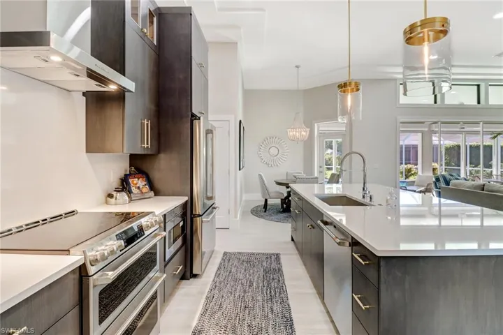 Kitchen featuring wall chimney range hood, appliances with stainless steel finishes, pendant lighting, glass insert cabinets, and open floor plan