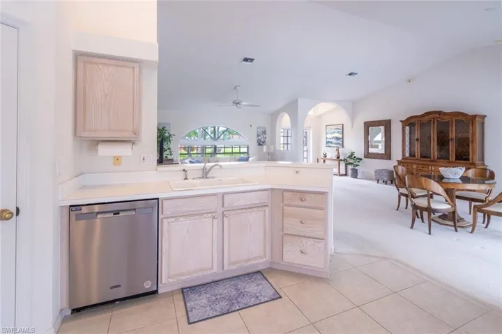 Kitchen with vaulted ceiling, stainless steel dishwasher, light tile patterned flooring, light brown cabinetry, and ceiling fan