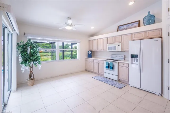 Kitchen featuring lofted ceiling, white appliances, light tile patterned floors, ceiling fan, and light brown cabinetry