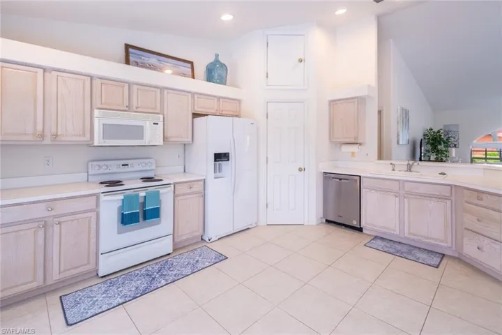 Kitchen featuring light brown cabinetry, high vaulted ceiling, sink, and white appliances