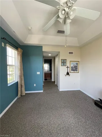 Carpeted master bedroom with ceiling fan and a tray ceiling