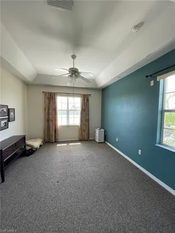 Carpeted master bedroom with ceiling fan and a tray ceiling