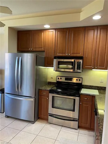 Kitchen featuring stainless steel appliances, dark stone counters, and light tile floors