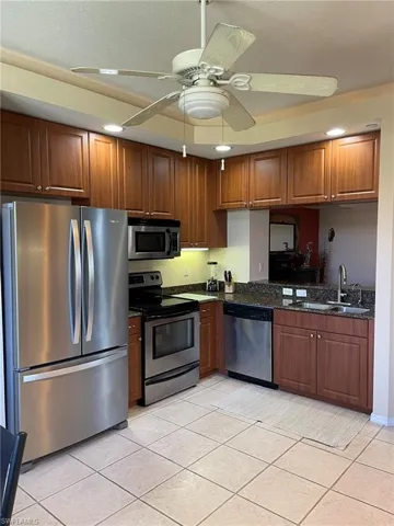 Kitchen with light tile flooring, stainless steel appliances, ceiling fan, dark stone countertops, and sink