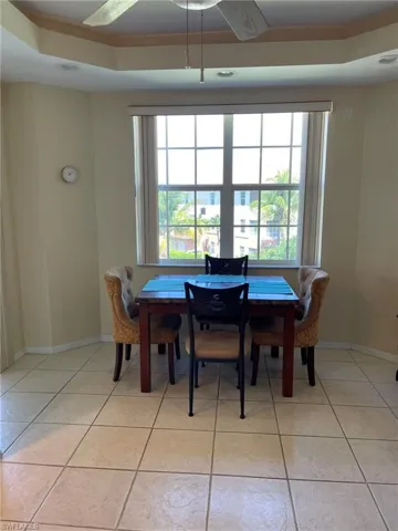 Eat-in kitchen with a raised ceiling, ceiling fan, and light tile flooring