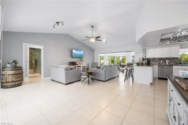 Tiled living room featuring ceiling fan, high vaulted ceiling, and track lighting