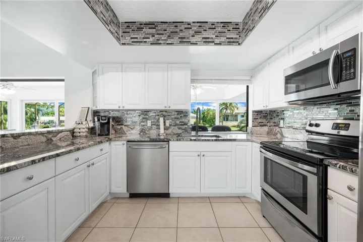 Kitchen with sink, decorative backsplash, ceiling fan, stainless steel appliances, and white cabinets