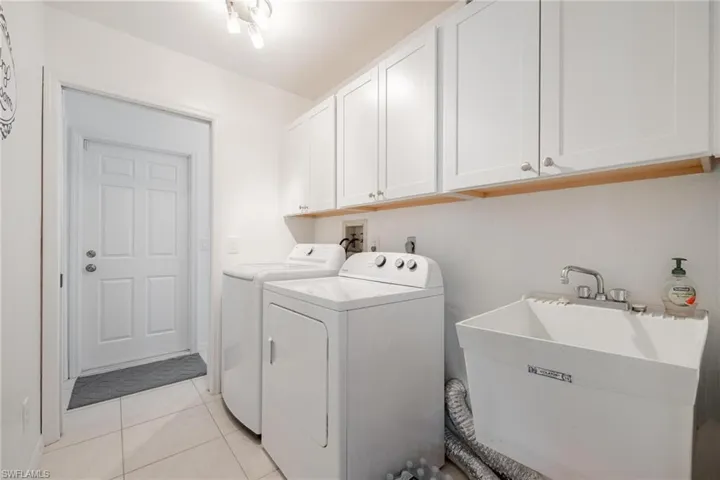 Laundry area featuring light tile patterned flooring, sink, separate washer and dryer, and cabinets