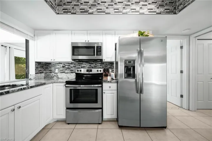 Kitchen with stainless steel appliances, stone counters, tasteful backsplash, white cabinets, and light tile patterned floors