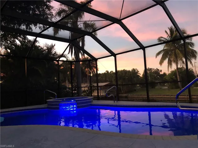Pool at dusk featuring a lanai and an in ground hot tub